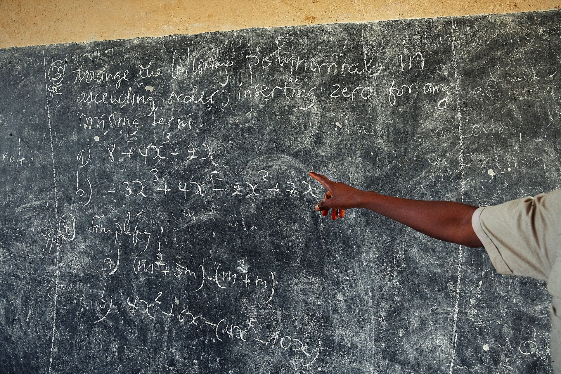 Teacher Hand pointing at blackboard with math problems in African school.
